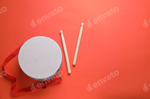 Preview: Toy drum and drumsticks on coral background, flat lay. Space for text