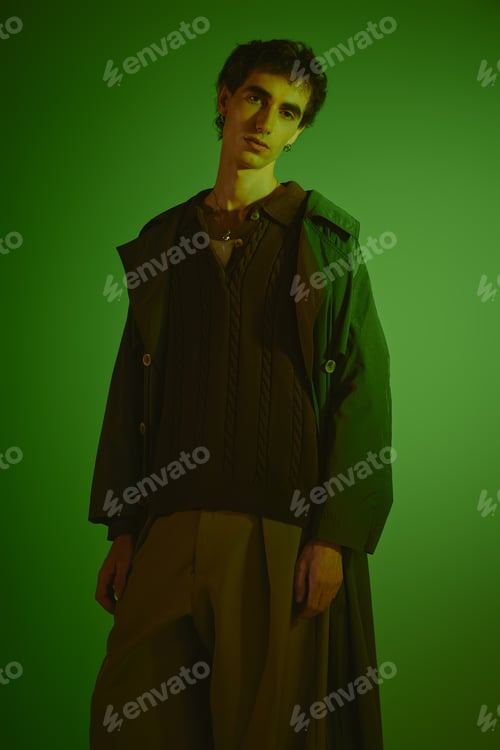 Preview: Young man showcases trendy fashion against a vibrant green backdrop in a striking pose