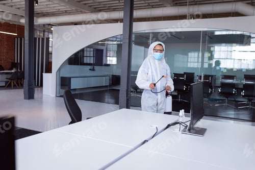 Preview: Cleaner wearing ppe suit, glasses and mask disinfecting office workspace