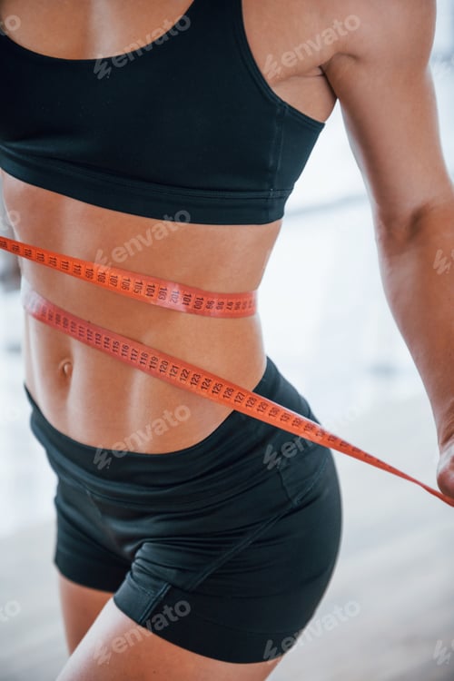 Preview: Close up view of woman's sportive body with measuring tape around waist