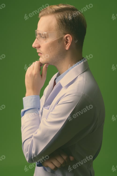 Preview: Young handsome man doctor with blond hair wearing protective glasses against green background