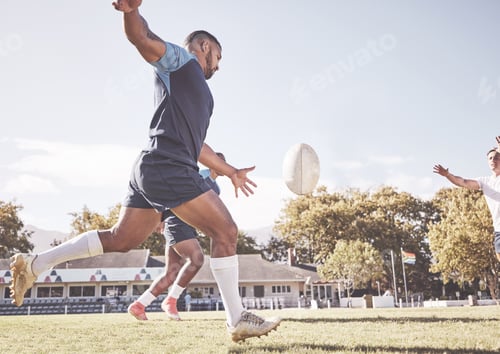 Preview: Mixed race rugby player attempting a dropkick during a rugby match outside on the field. Hispanic m
