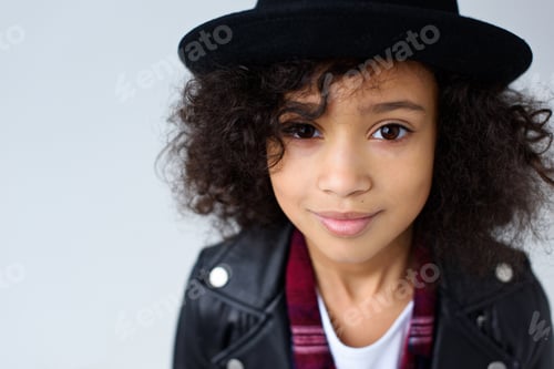 Preview: close-up portrait of beautiful little child in leather jacket and hat looking at camera isolated on