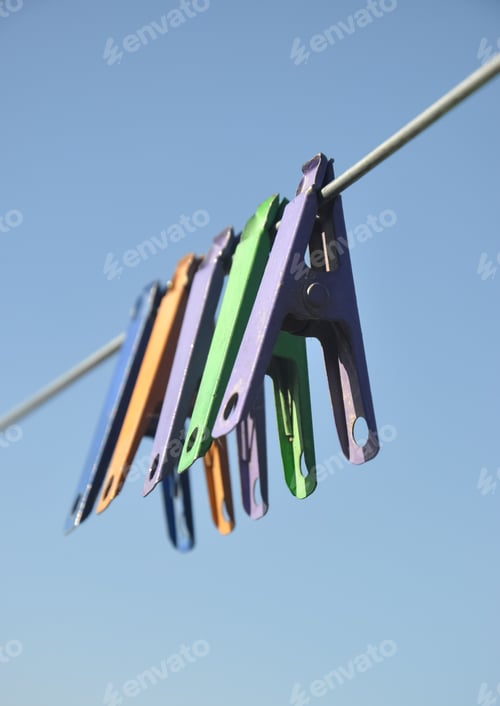 Preview: Low angle shot of multicolored cloth pins hanging on wire in outdoor with blue sky in background