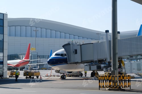 Preview: Airplanes at busy airport terminal with boarding bridge connecting to plane under clear blue sky