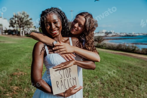Preview: Two women are hugging each other and holding a sign that says "Stop Racism"