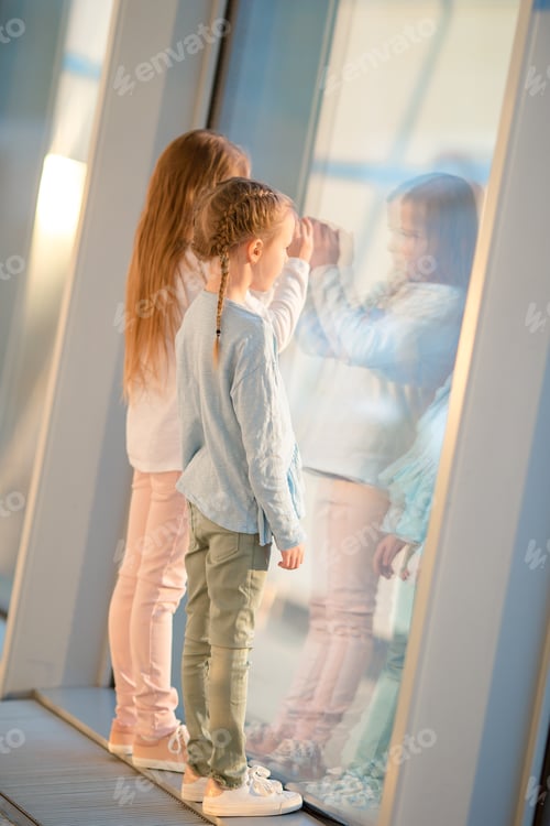 Preview: Little adorable girls in airport waiting for boarding near big window