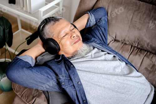 Preview: Asian Senior Man Lying On Sofa With Closed Eyes While Using Headphone