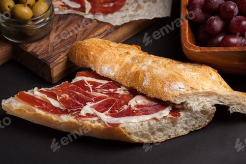 Preview: Jamon Iberico with white bread, olives on toothpicks and fruit on a dark background