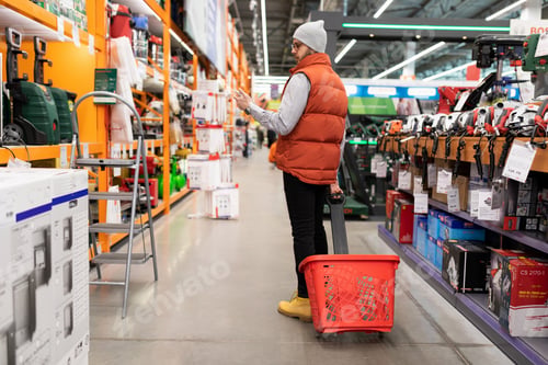 Preview: a male buyer in a hardware store with a basket walks between the rows of goods