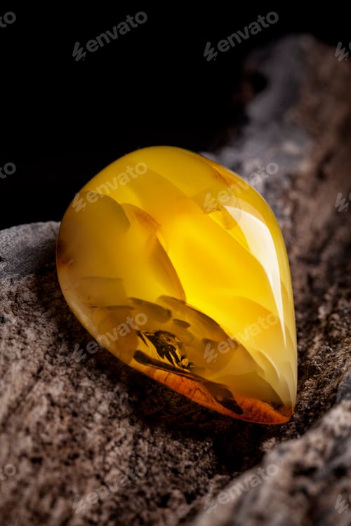 Preview: Natural amber. A piece of yellow opaque natural amber on large piece of dark stoned wood