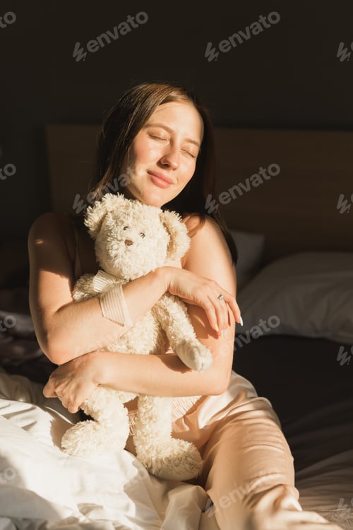 Preview: Girl is waking up in morning stretches in bed and sun shines from the window. Happy young woman