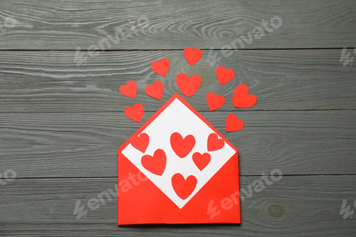 Preview: Valentine's Day. Envelope with many paper hearts on grey wooden background, top view