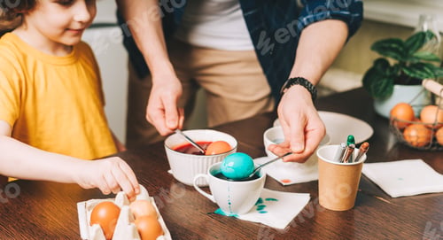 Preview: Easter day. Close up hands of Father and son painting eggs on wooden background. Family sitting in a