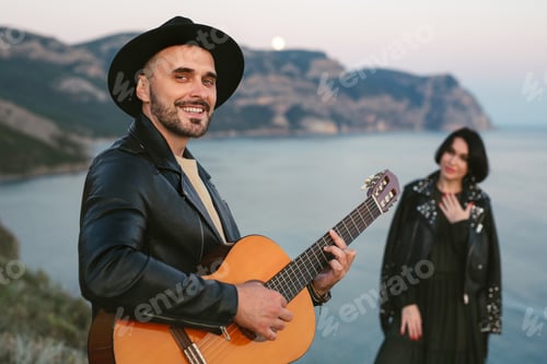 Preview: Couple in love on top of a mountain overlooking the sea. A man in a hat plays the guitar.