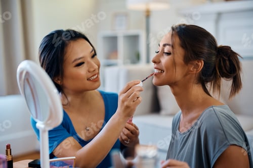 Preview: Happy female friends applying make up at home.
