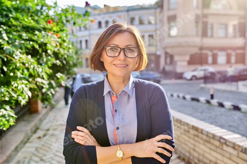 Preview: Outdoor portrait of smiling mature business woman wearing glasses with crossed arms