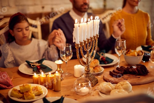 Preview: Close-up of lighted candles in menorah with Jewish family saying grace in the background.