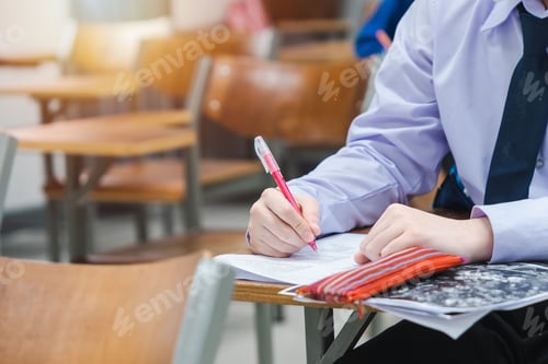 Preview: Closeup shot of a college student writing on a paper in a classroom on an isolated background