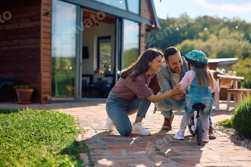Preview: Happy parents having fun while teaching their daughter to ride bicycle.