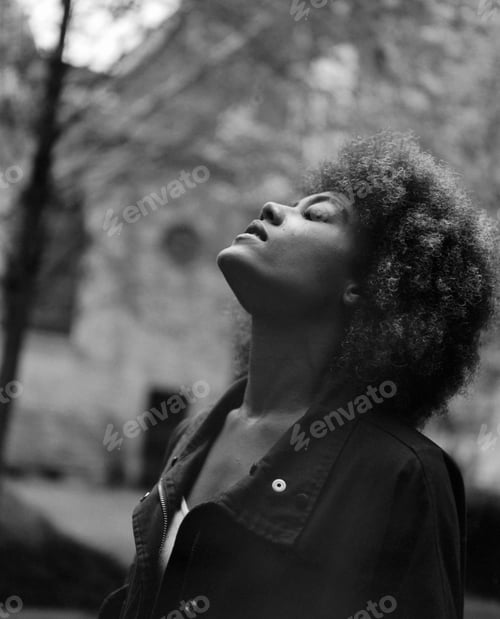 Preview: Monochrome image of curly woman with eyes closed outdoors.