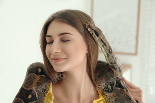 Preview: Young woman with boa constrictor at home. Exotic pet