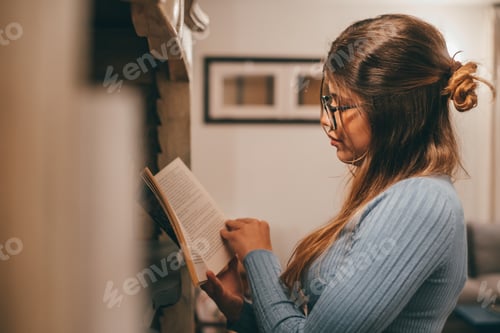 Preview: One cute and attractive wearing eye glasses reading and looking an interesting book at home indoor.