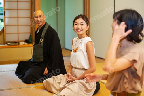 Preview: Two Japanese women and Buddhist priest kneeling in Buddhist temple, talking.