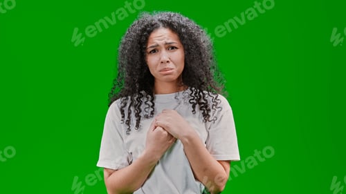 Preview: Young and sad African American woman staring at the camera in front of a green wall