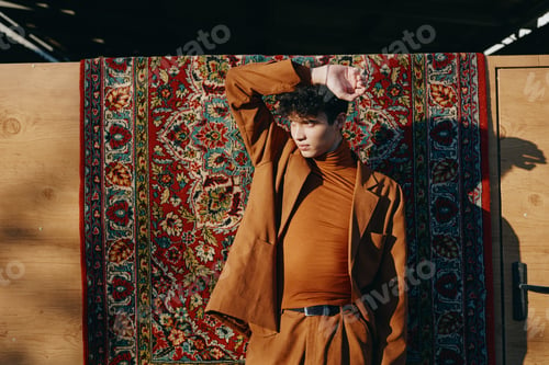 Preview: Stylish young man posing against a vibrant, patterned rug background, showcasing contemporary