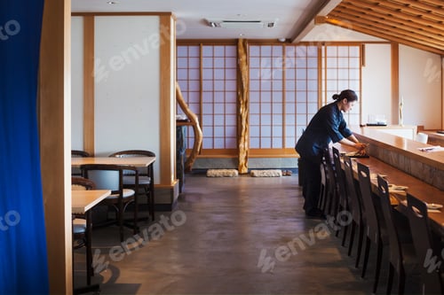 Preview: Waitress standing at a counter in a Japanese sushi restaurant, preparing place settings.