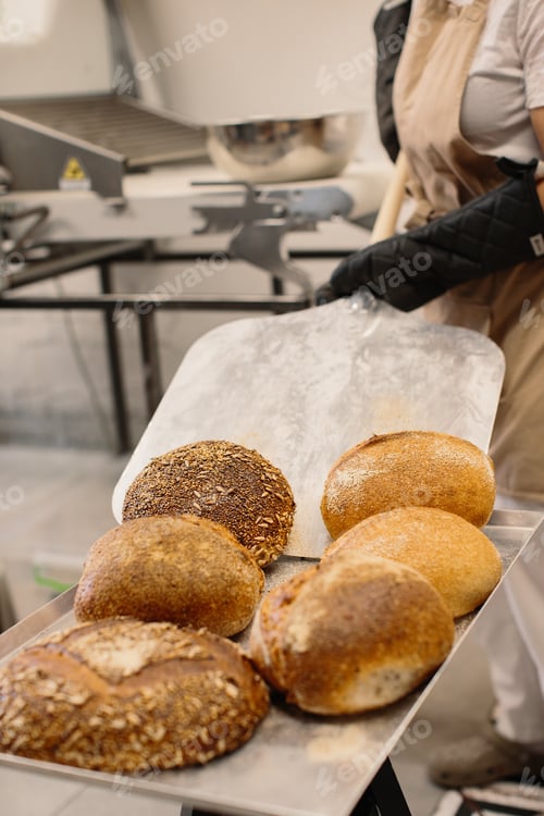 Preview: Female baker using a peel to take out a loaf of bread of the oven in a bakery