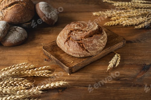 Preview: Round freshly baked bread on a wooden board in the center, ears of wheat diagonally.