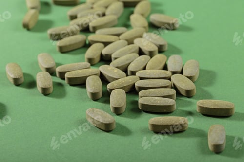 Preview: Herbal and Vitamin Green pills freely laid on green background