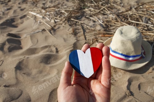 Preview: wooden heart in hands with colors of flag France blue white and red on sand straw hat with ribbon