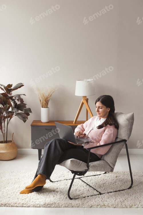 Preview: Attractive confident woman working remote on laptop from home with trendy interior