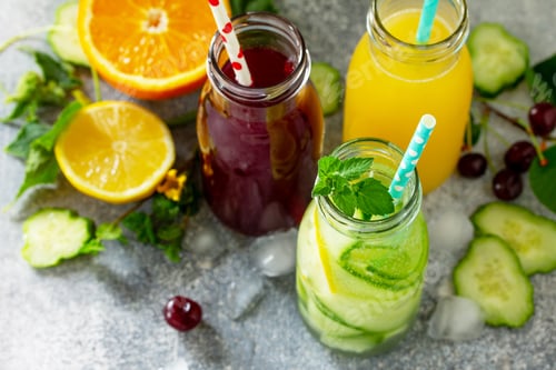 Preview: Various refreshments drinks - detox cucumber water, cherry juice and orange juice on stone table.