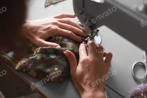 Preview: Seamstress working on modern electrical sewing machine making exclusive garments in fashion studio.