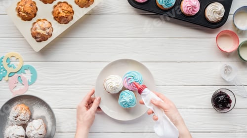 Preview: partial view of woman decorating cupcakes with icing bag on table with cupcake trays