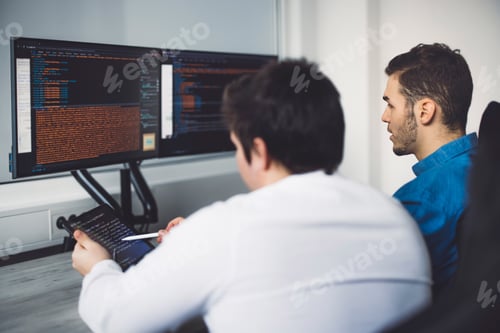 Preview: View from the back two male IT programmers working on desktop computers and a tablet, coding