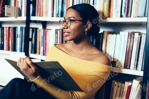 Preview: Smart student reading book beside bookcase