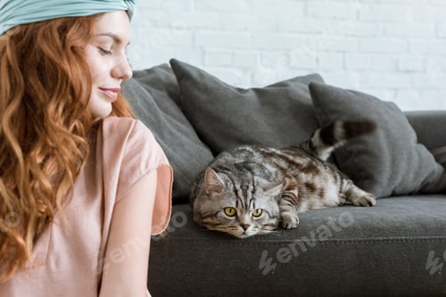 Preview: attractive young woman smiling at adorable tabby cat at home