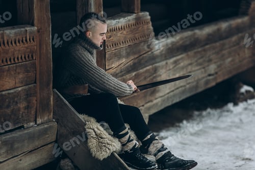 Preview: Portrait of strong viking warrior sharpening his sword, scandinavian viking cosplay