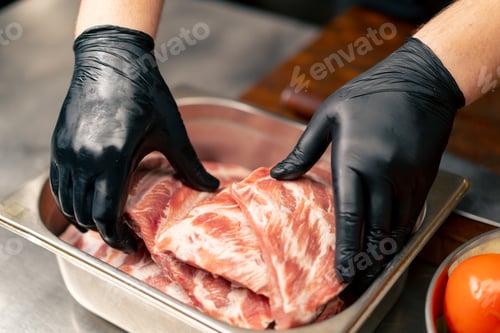 Preview: in professional kitchen hands in black gloves take ribs from a bowl and transfer them to a board