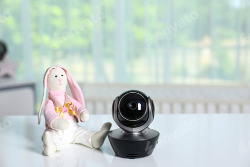 Preview: Baby camera with toy on table in room, space for text. Video nanny
