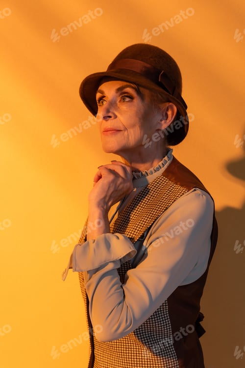 Preview: Senior woman in stylish vintage clothes looking away on orange background