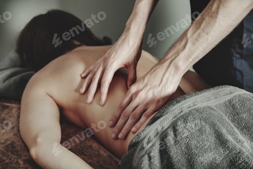 Preview: Masseur hands doing back massage in medical office of fitness room for woman