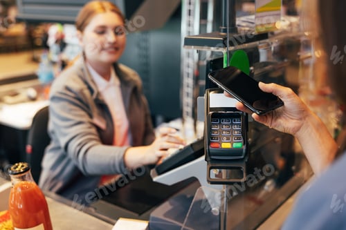 Preview: Unrecognizable woman paying by phone at the counter in a grocery store