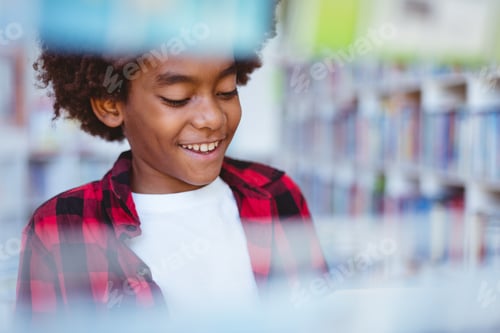 Preview: Laughing african american schoolboy reading book standing in school library