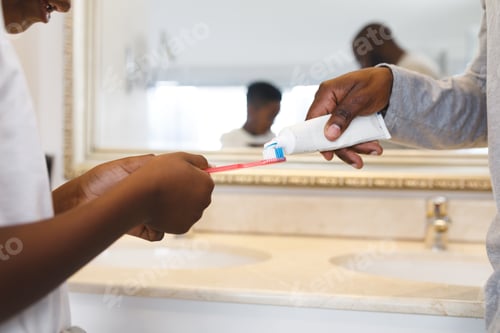 Preview: African american father and son putting toothpaste on toothbrush in bathroom